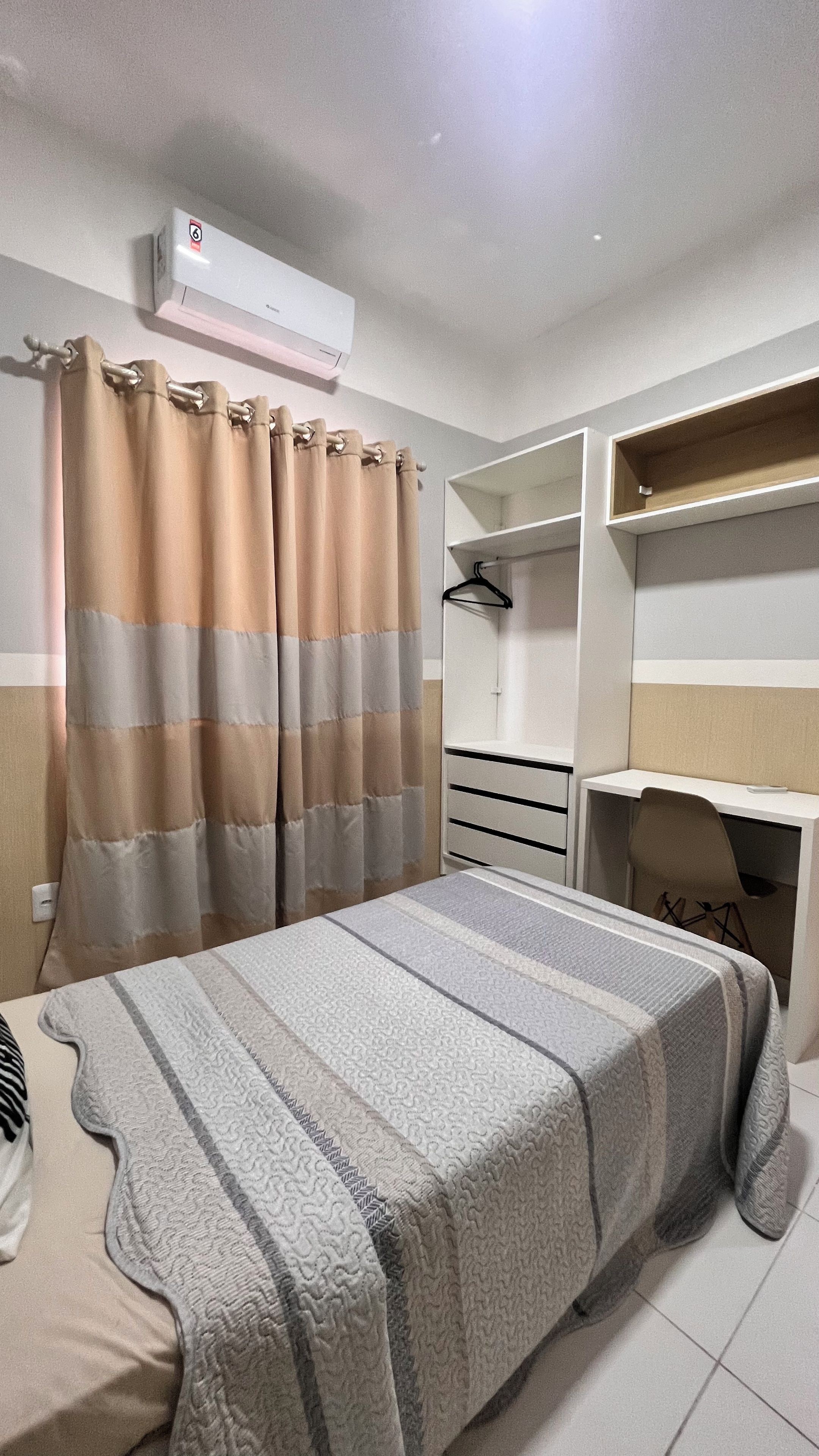 A bedroom with a bed, a desk, a wardrobe, and a hanging space.