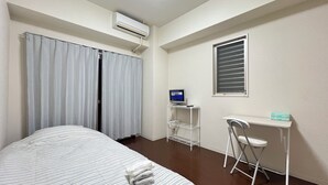 Habitación de hotel con cama, escritorio con computadora, ventana con persianas y aire acondicionado.