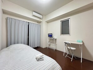 Ein Hotelzimmer mit einem Bett, einem Schreibtisch mit Computer, einem Fenster mit Jalousien und einer Klimaanlage.