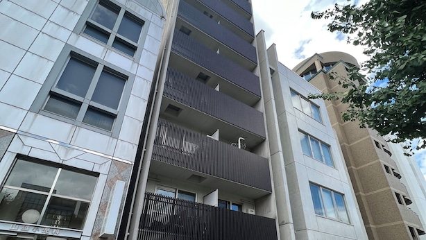 Un edificio de varios pisos con diseño arquitectónico moderno, que destaca por una entrada imponente con fachada de vidrio y portón metálico.