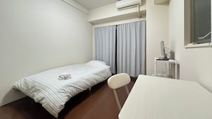 Una habitación pequeña y limpia con una cama individual, un escritorio y un aire acondicionado.