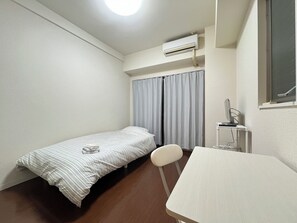 A small, clean room with a single bed, a desk, and an air conditioning unit.