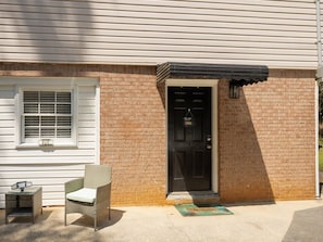 A house with a black door, a window with blinds, a chair, and a small table outside. - Pine View Corner - GA (Riverdale)