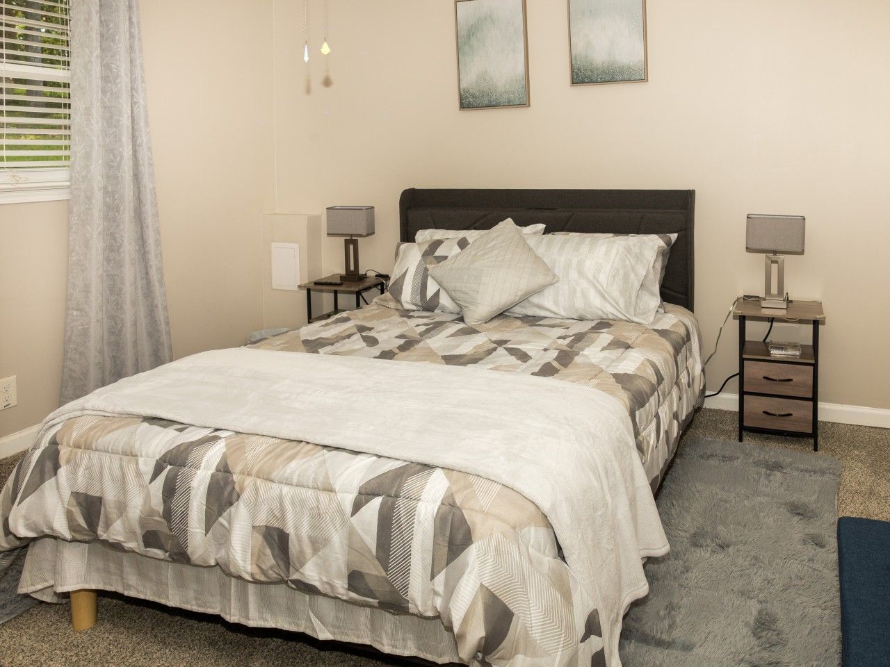 A bedroom with a bed, two bedside tables, a nightstand, a rug, and a window with curtains.