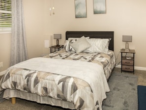 A bedroom with a bed, two bedside tables, a nightstand, a rug, and a window with curtains. - Pine View Corner - GA (Riverdale)