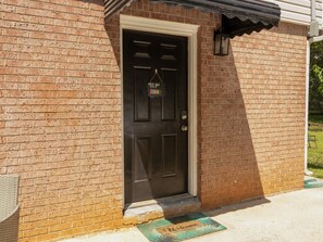 A brick building with a dark brown door, a metal doorbell, and a green mat at the entrance. - Pine View Corner - GA (Riverdale)