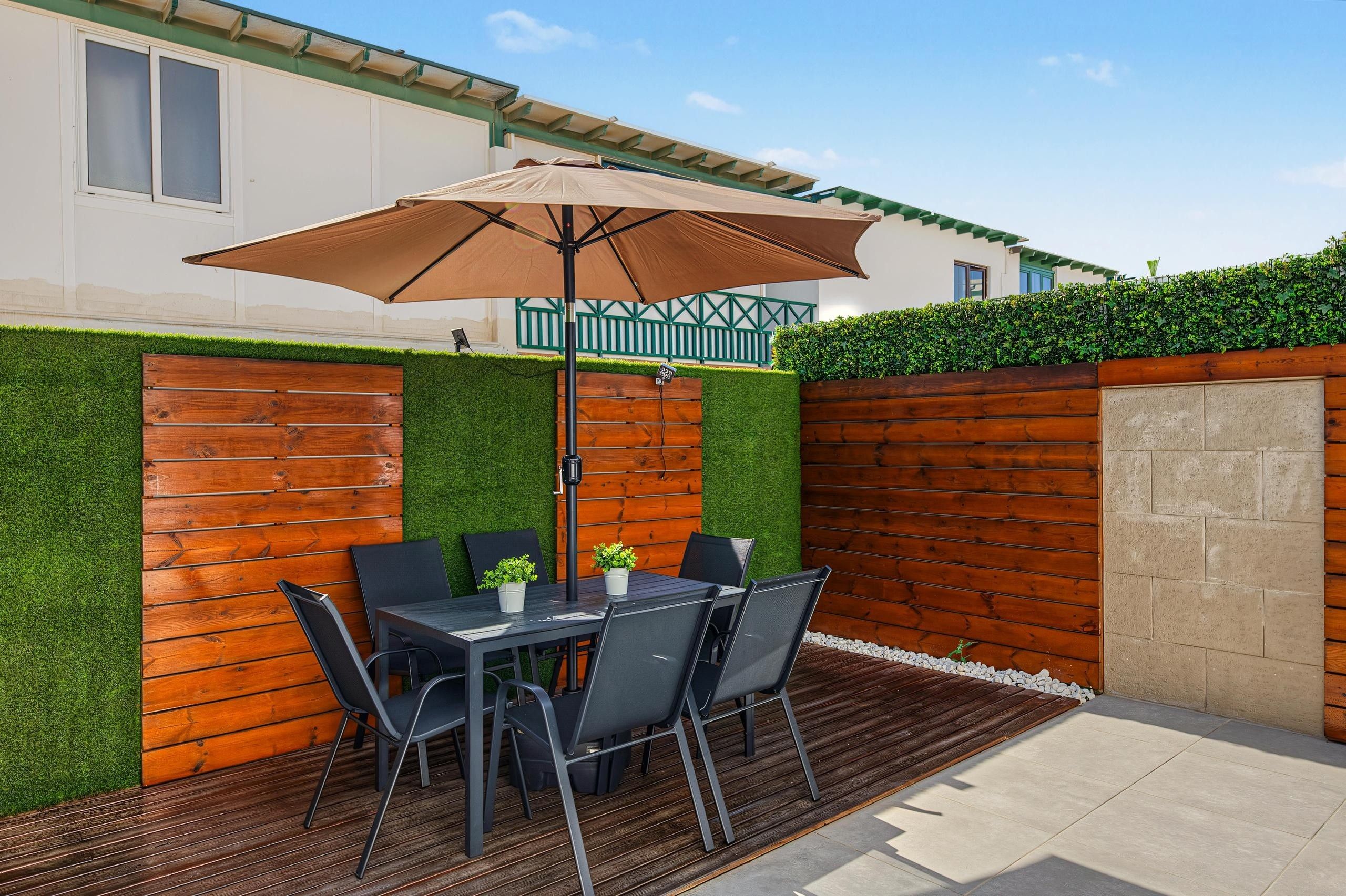 A patio with a table and chairs, a large umbrella, and a wooden fence.