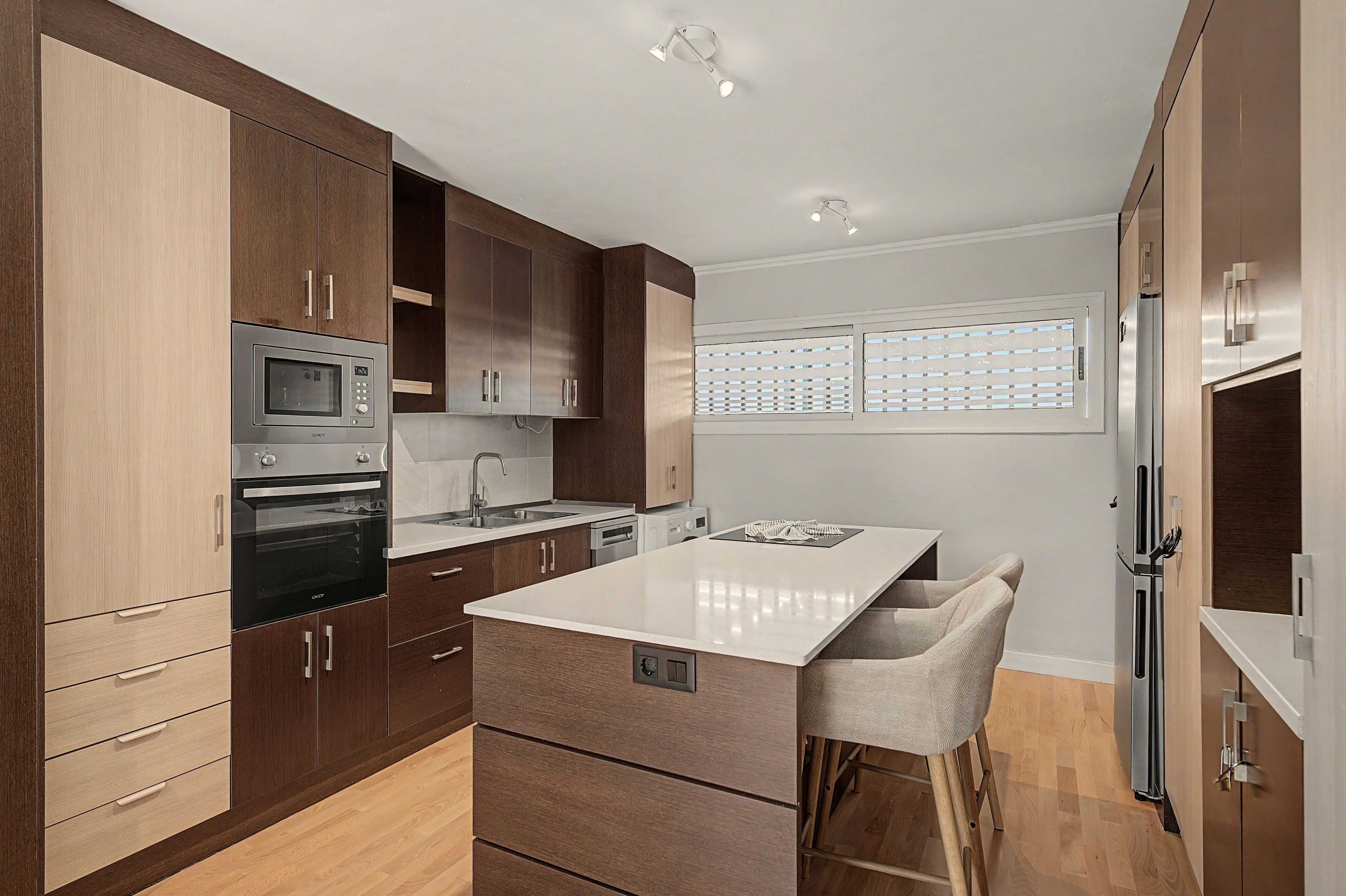 A modern kitchen with wooden cabinets, stainless steel appliances, a central island, and a window with blinds.