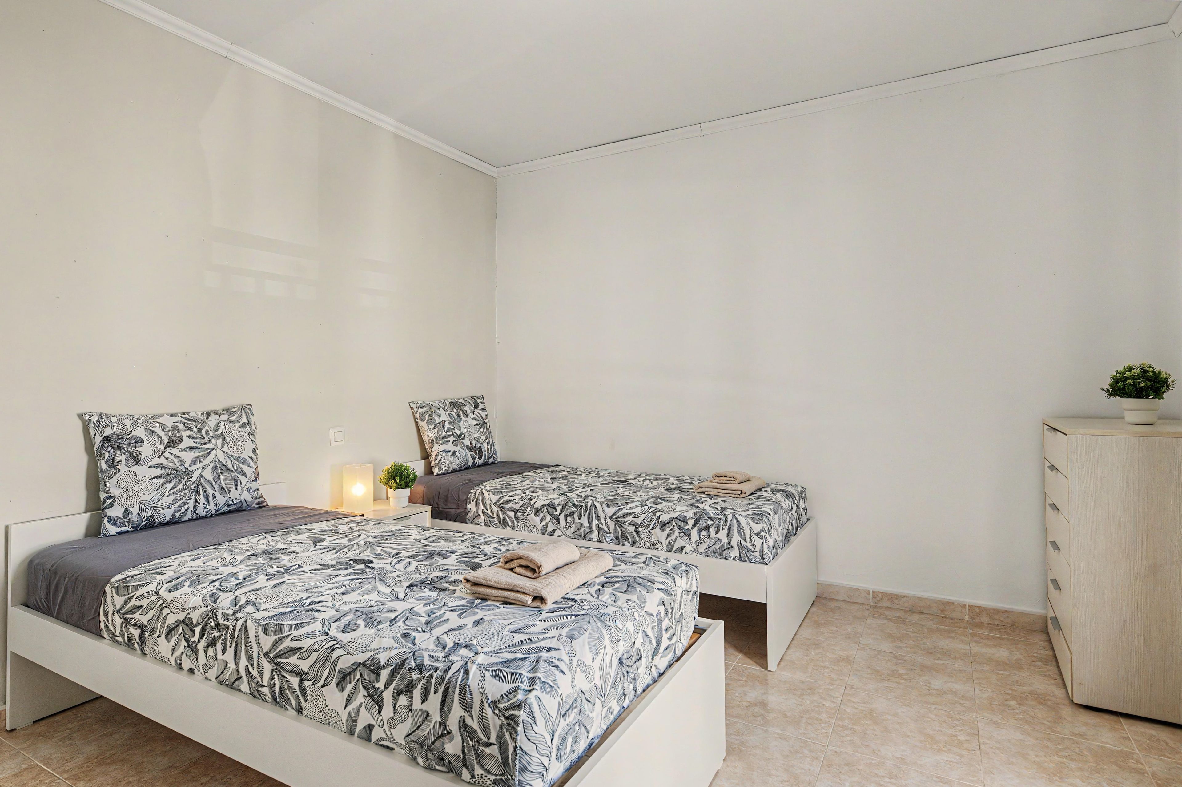 A bedroom with two beds, each with patterned bedding, a bedside table with a lamp, and a cabinet.