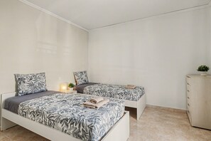 Ein Schlafzimmer mit zwei Betten, jeweils mit gemusterten Bettbezügen, einem Nachttisch mit Lampe und einem Schrank.