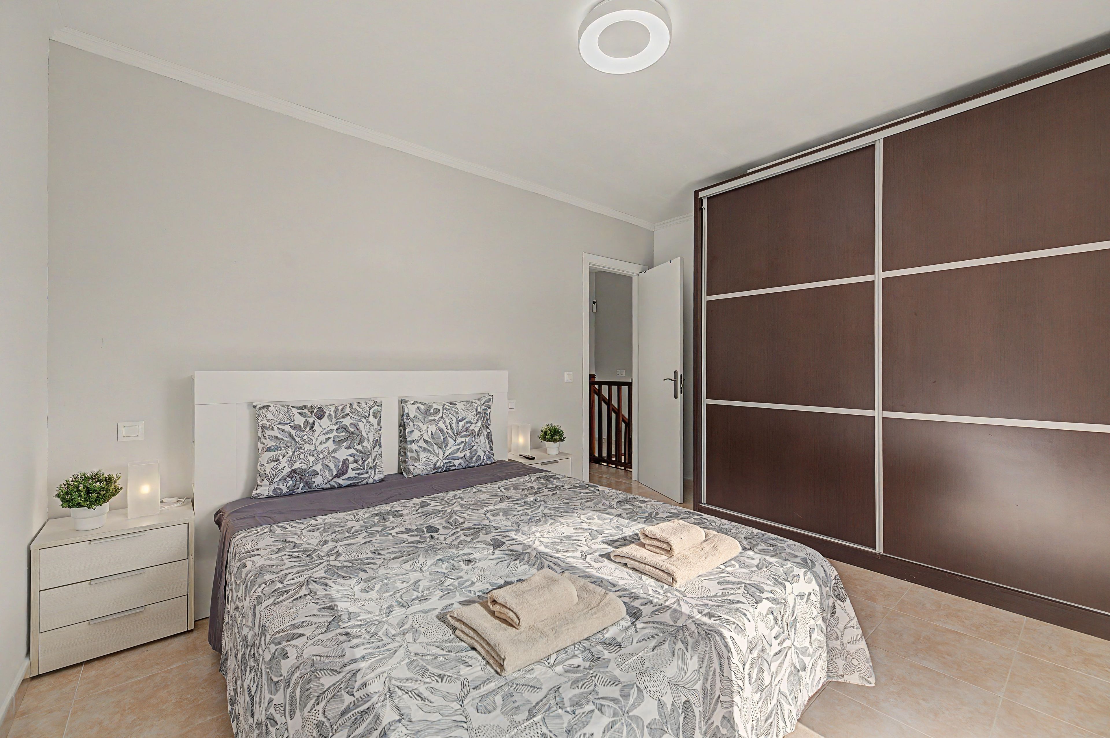 A bedroom with a bed, bedside tables, a wardrobe, and a potted plant.