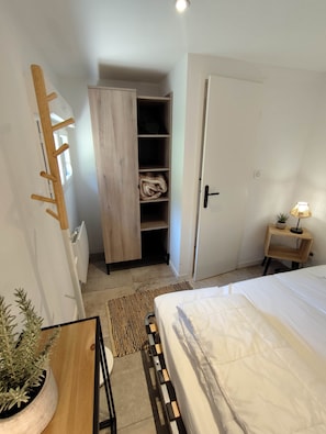A bedroom with a bed, a wooden wardrobe, a small table with a plant, and a bedside lamp.