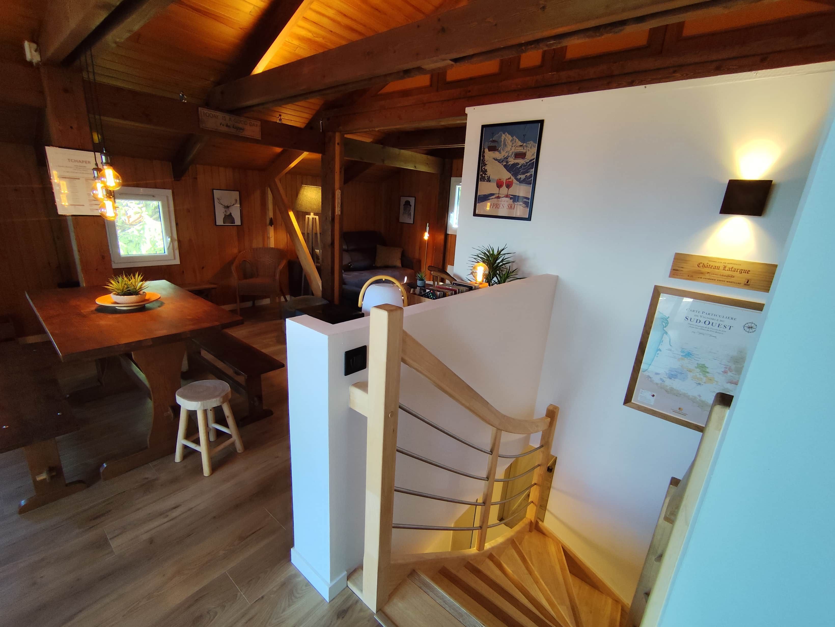 Un intérieur en bois comprenant un escalier, un coin repas et un mur où sont accrochés des certificats encadrés.