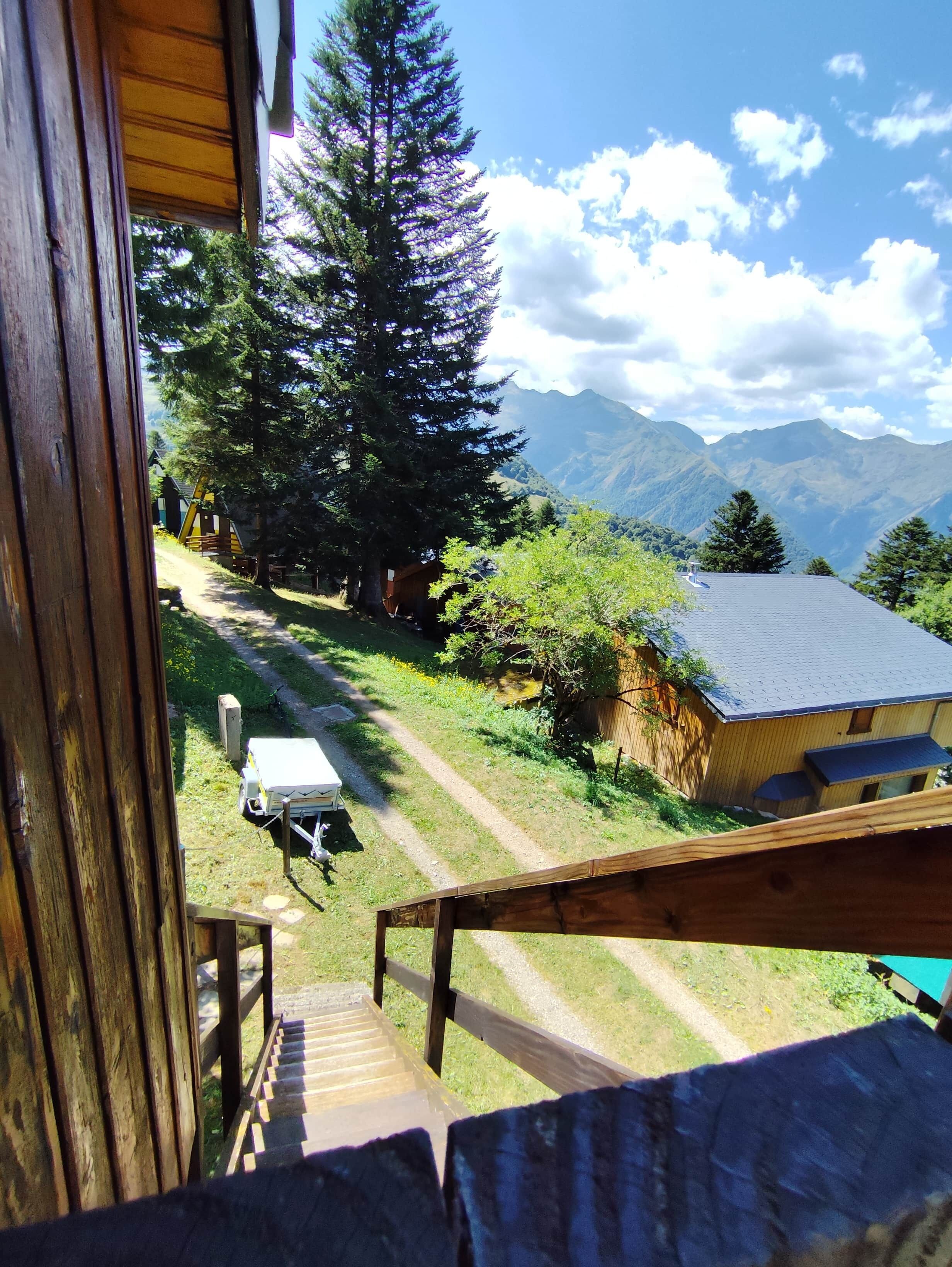 Une terrasse en bois mène à un chalet offrant une vue sur une chaîne de montagnes et une zone boisée.