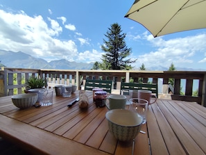 A wooden deck with a table set for dining, overlooking a mountainous landscape.