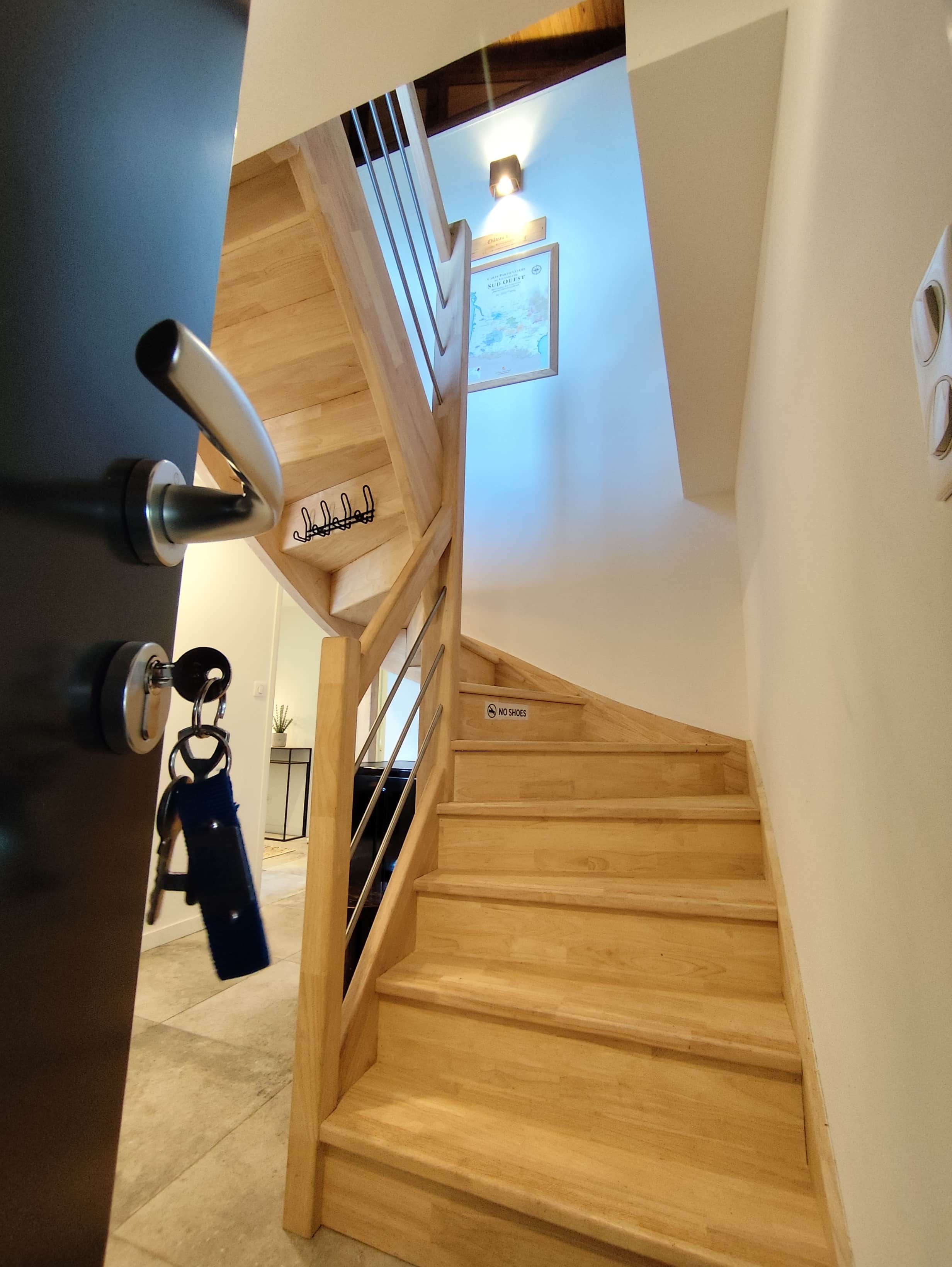 Een houten trap met een 'GEEN SNEAKERS'-bordje, een deur met een sleutel slot en een wandlamp.