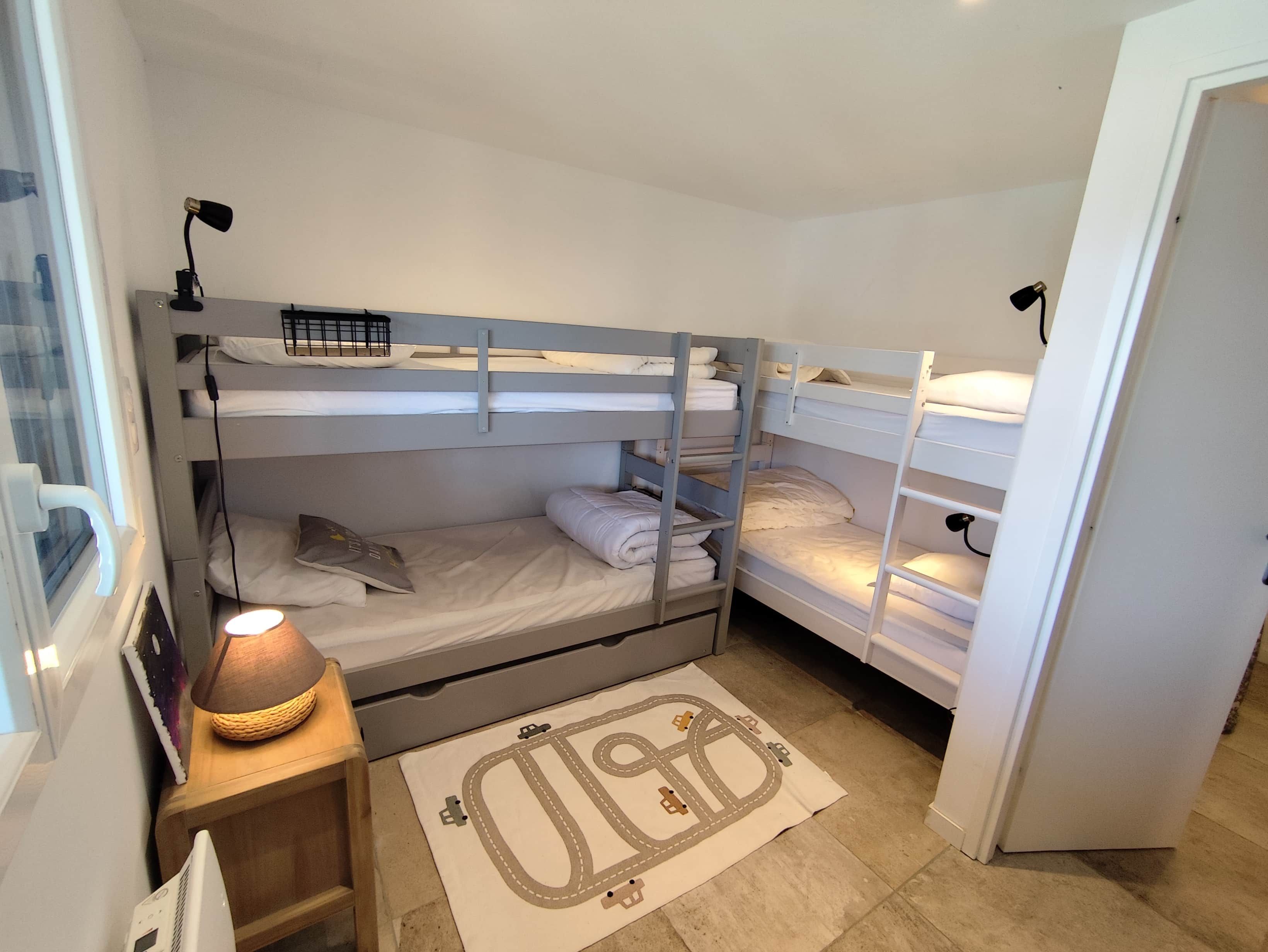 A room with bunk beds, a bedside table with a lamp, and a rug with a road and car design.
