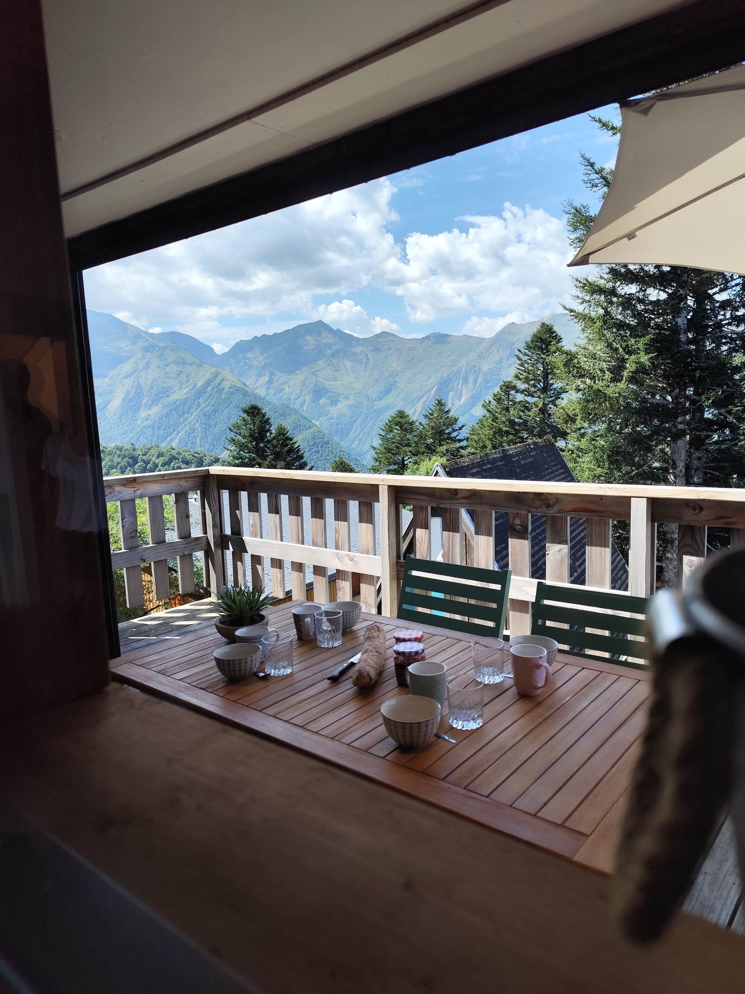 A wooden deck with a table set for dining, overlooking a mountainous landscape.
