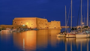 Un'antica fortezza in pietra con un fossato, circondata da acque calme e imbarcazioni ormeggiate.