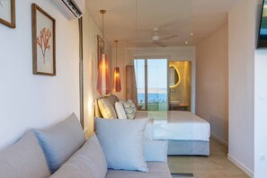 Ein modernes Hotelzimmer mit einer Couch, zwei Betten, einem großen Fenster und einem Badezimmer mit Spiegel und Waschbecken.