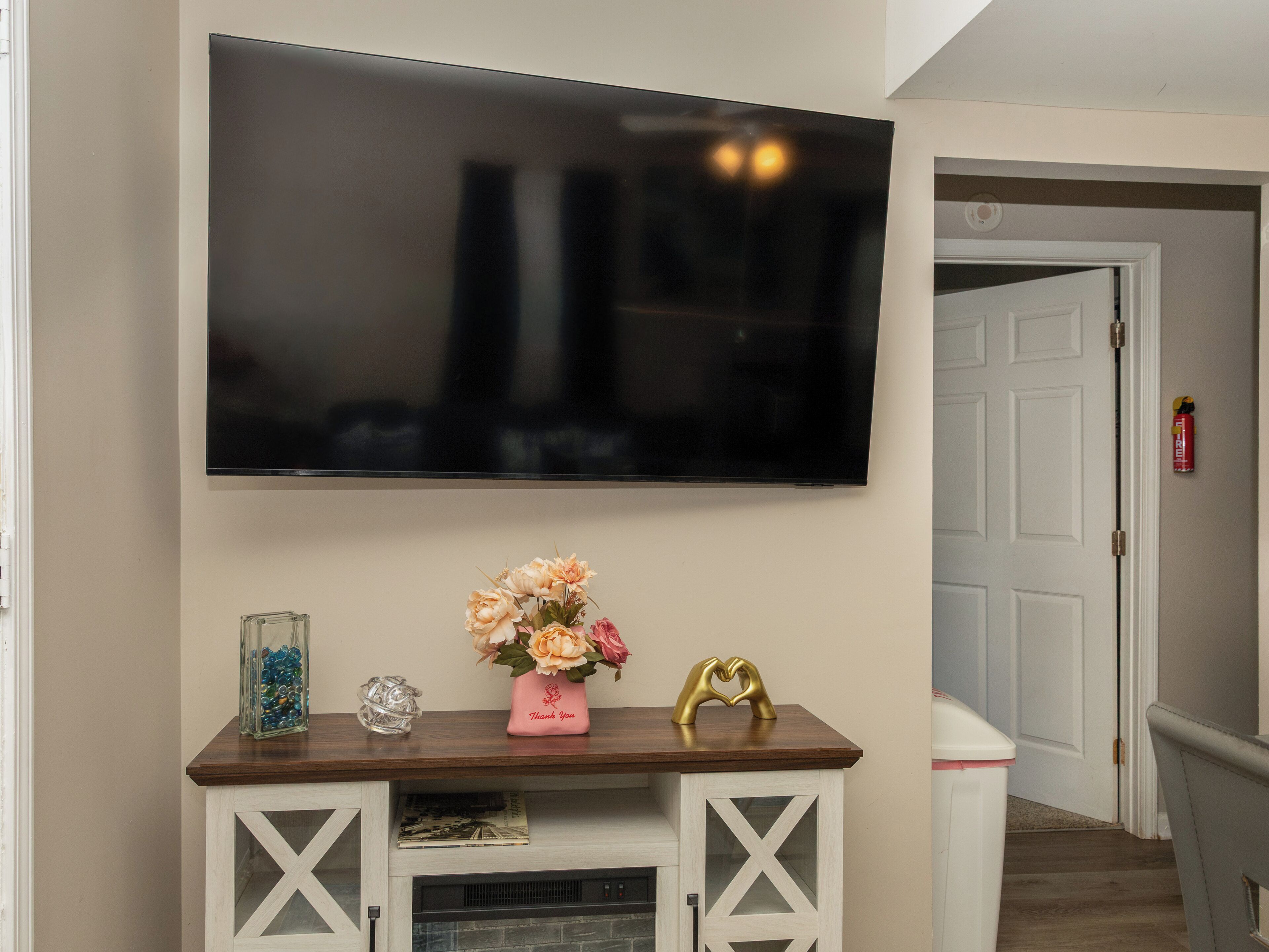Uma TV de tela plana fixada na parede acima de um console de madeira com objetos decorativos.