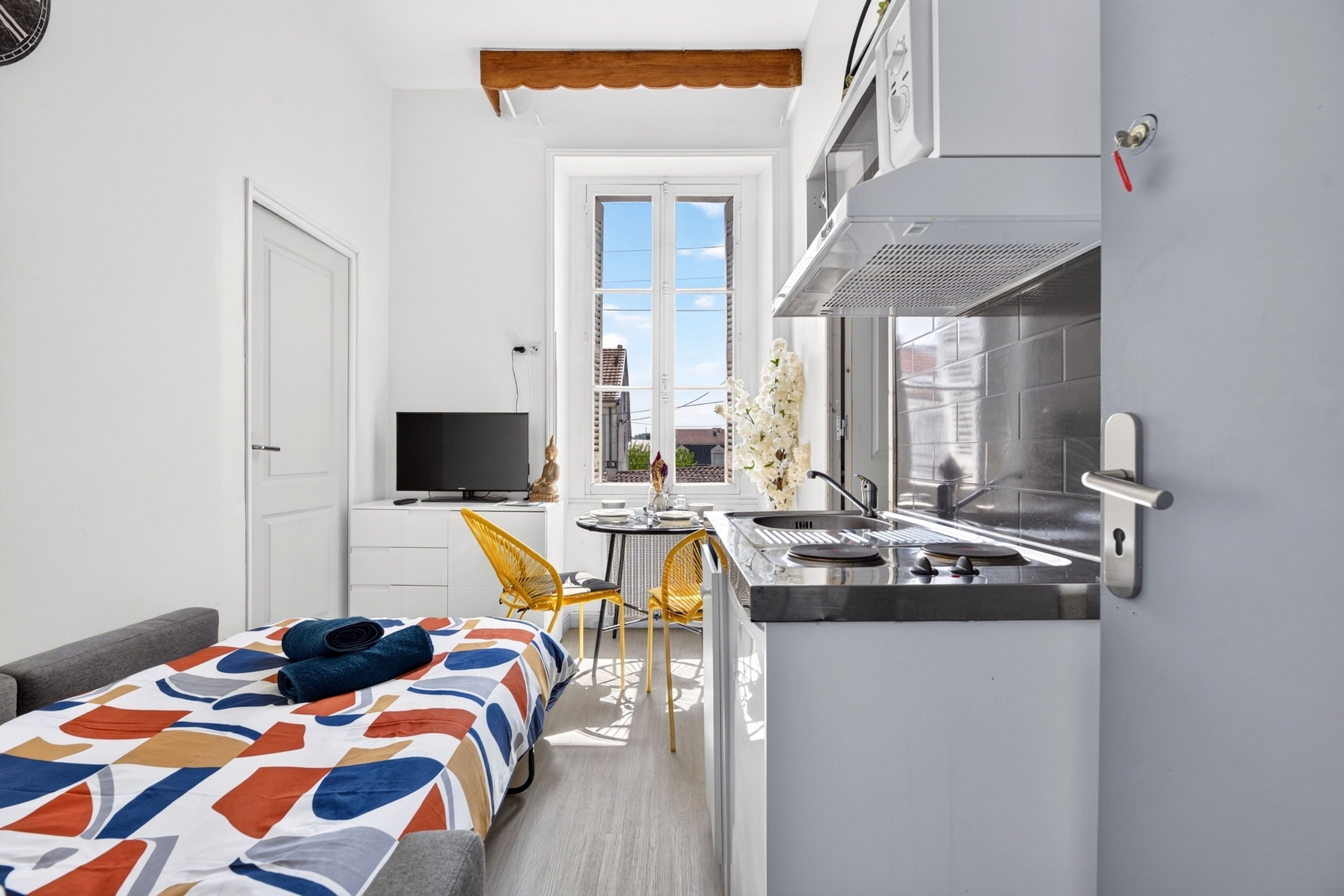 A compact kitchen with a built-in stove, a dining area with a small table and chairs, and a sofa with a patterned cover.