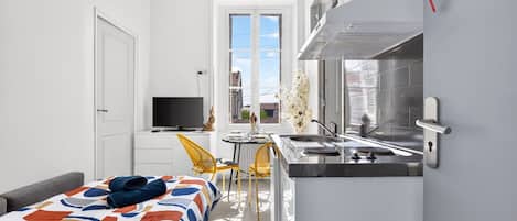 A compact kitchen with a built-in stove, a dining area with a small table and chairs, and a sofa with a patterned cover.