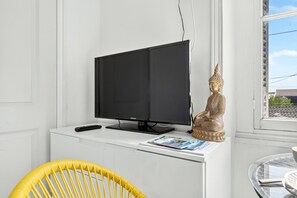A television on a white stand, a golden Buddha statue, and a yellow chair. - Tibet - Studio pour 3personnes (Périgueux)