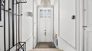 Un passadís blanc amb una porta doble, un petit finestral amb reixes de ferro decoratives i una làmpada sobre la porta.
