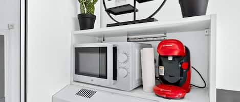 Een keuken met een magnetron, een rode koffiezetapparaat en planten in potten op een plank.