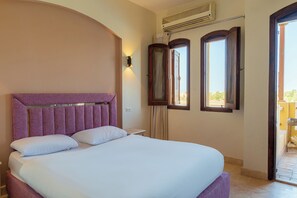 Ein Hotelzimmer mit einem großen Bett, einer Wandklimaanlage und Blick durch eine offene Tür.