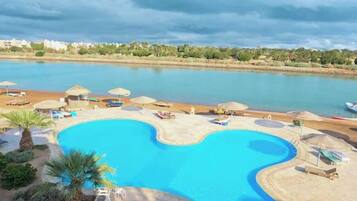 A swimming pool with a curved edge, surrounded by lounge chairs and umbrellas, with a view of a body of water and distant buildings.