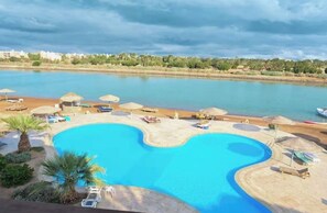 Ein Pool mit geschwungener Kante, umgeben von Liegestühlen und Sonnenschirmen, mit Blick auf ein Gewässer und entfernte Gebäude.