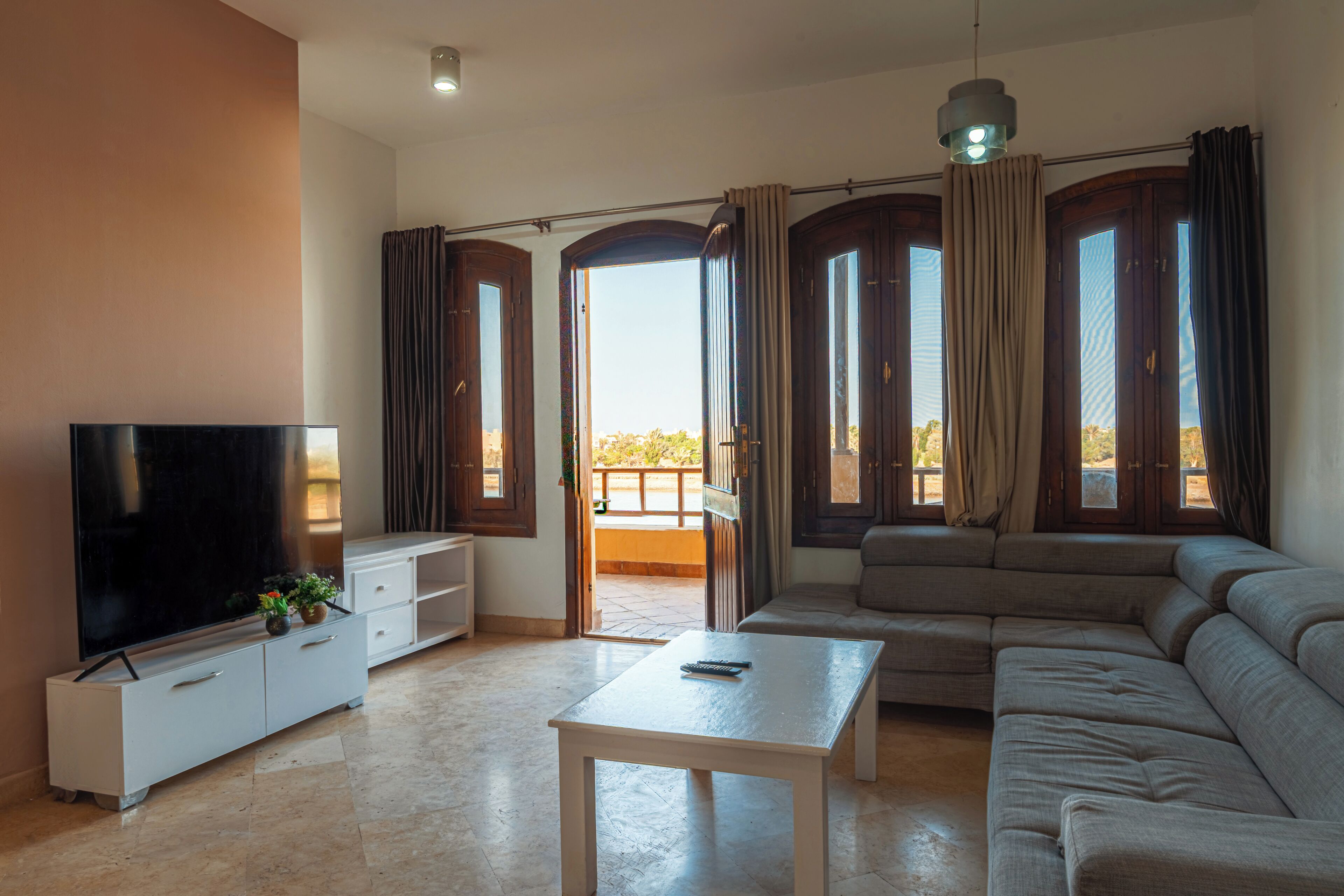 A living room with a flat-screen TV, a sofa, a coffee table, and a balcony with curtains.