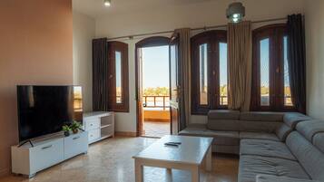 A living room with a flat-screen TV, a sofa, a coffee table, and a balcony with curtains.