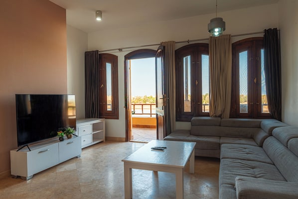 Una sala de estar con televisor de pantalla plana, un sofá, una mesa de centro y un balcón con cortinas.