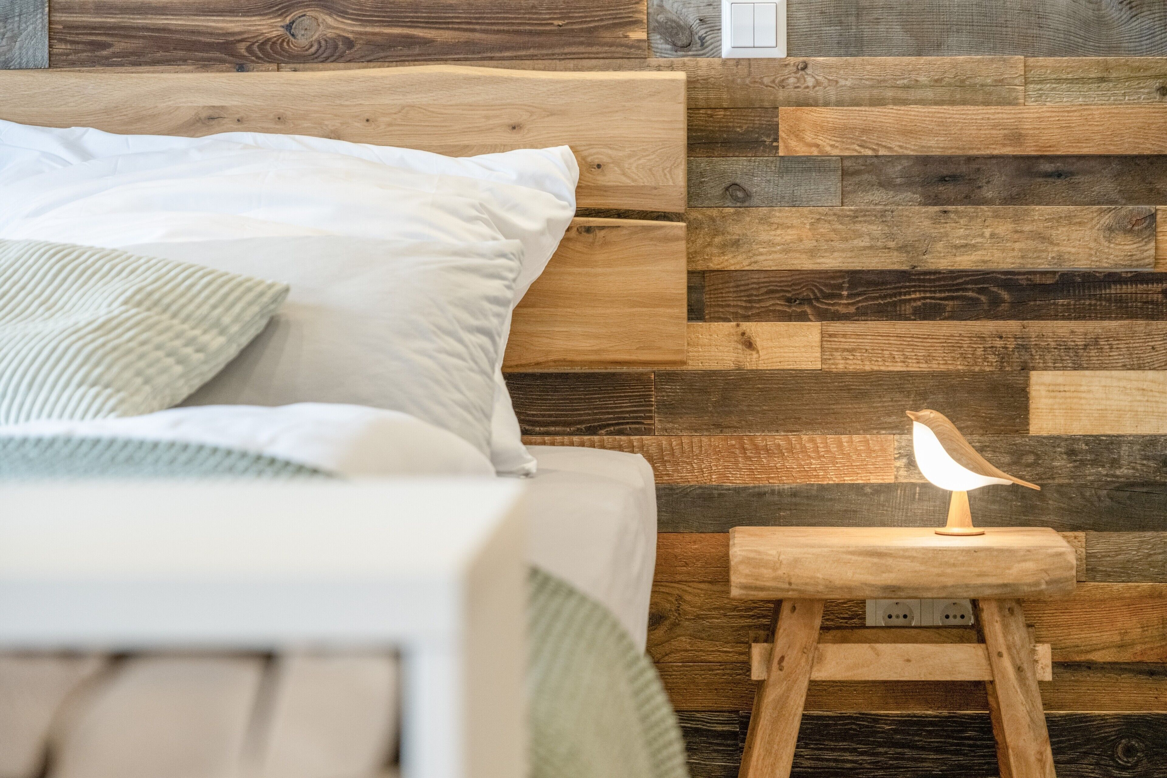 Un lit avec des oreillers, une tête de lit en bois et une table de chevet avec une lampe et une petite sculpture en bois.