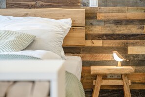 Una cama con almohadas, cabecera de madera y mesita de noche con lámpara y una pequeña escultura de madera.