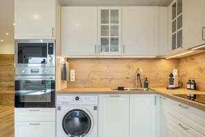 Una cocina moderna con electrodomésticos de acero inoxidable, horno empotrado, lavadora y armarios de madera.