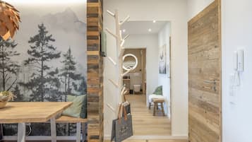 Un interno moderno con un tavolo da pranzo in legno, un appendiabiti e una parete con un murale raffigurante montagne e alberi.