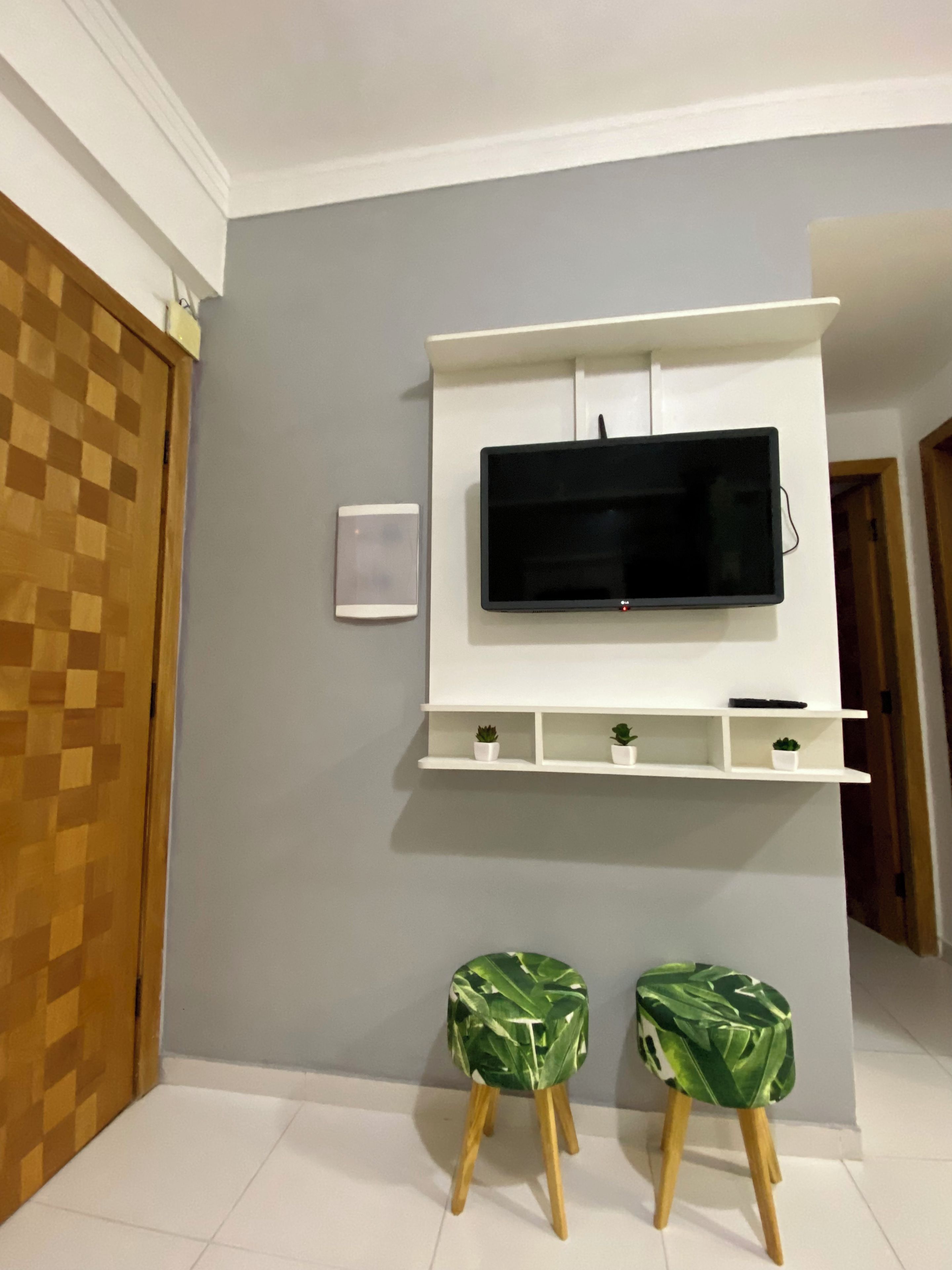 Una sala de estar con un televisor montado, dos taburetes y una puerta de madera.