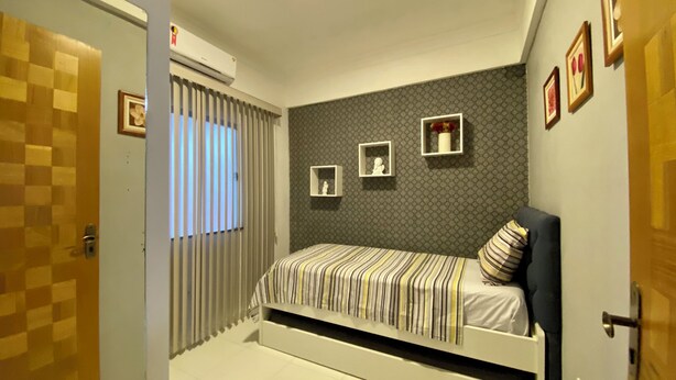 Un dormitorio con cama, ventana con persianas, aire acondicionado de pared y cuadros enmarcados.
