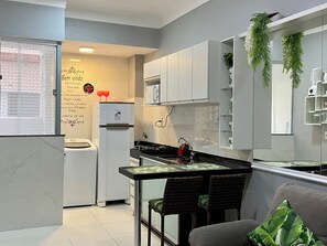 Une cuisine moderne avec des meubles blancs, un réfrigérateur, un four à micro-ondes et un coin repas comprenant une table et des chaises.