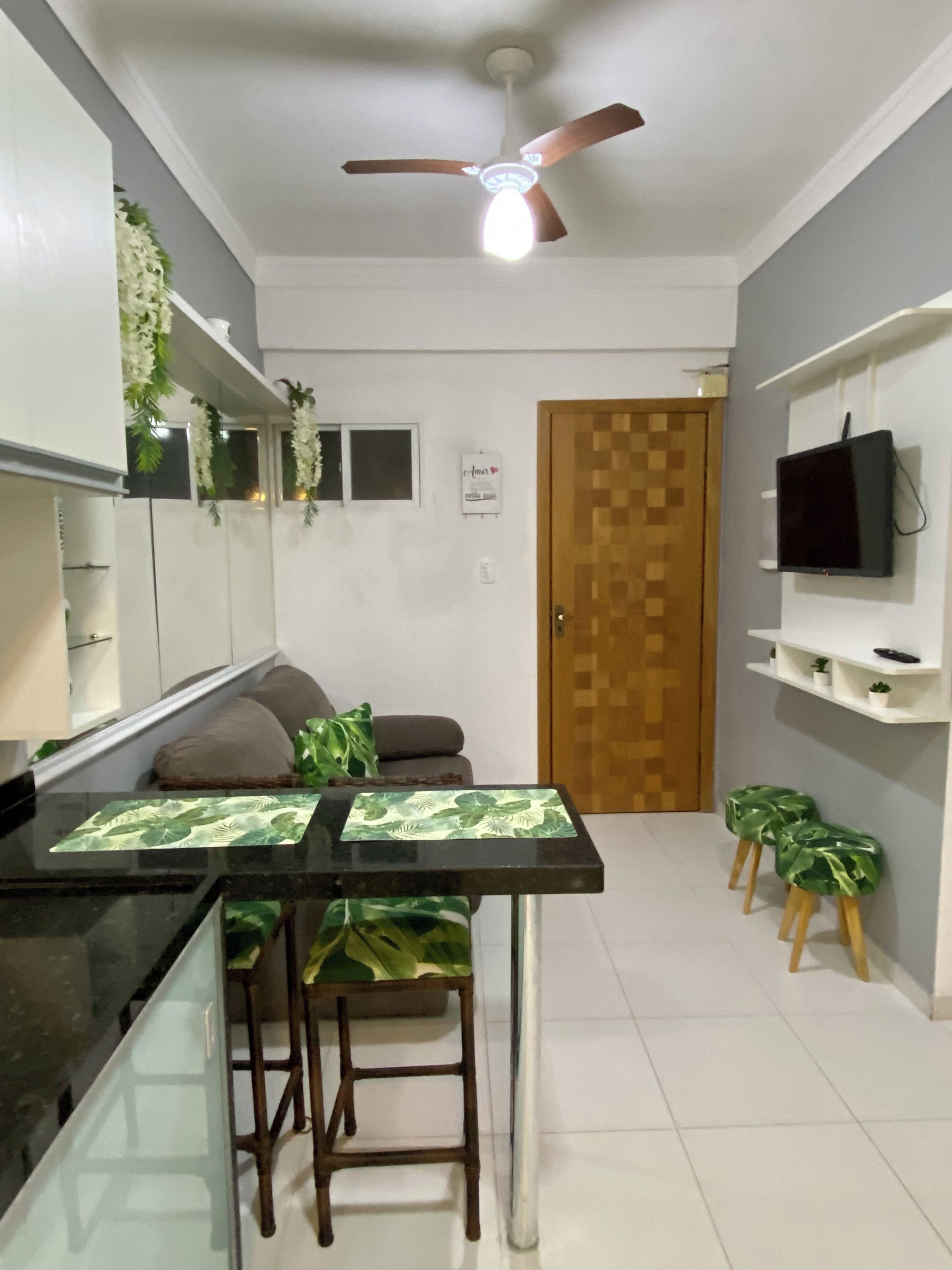 Una cocina compacta con comedor, ventilador de techo, televisor y puerta con diseño de madera.