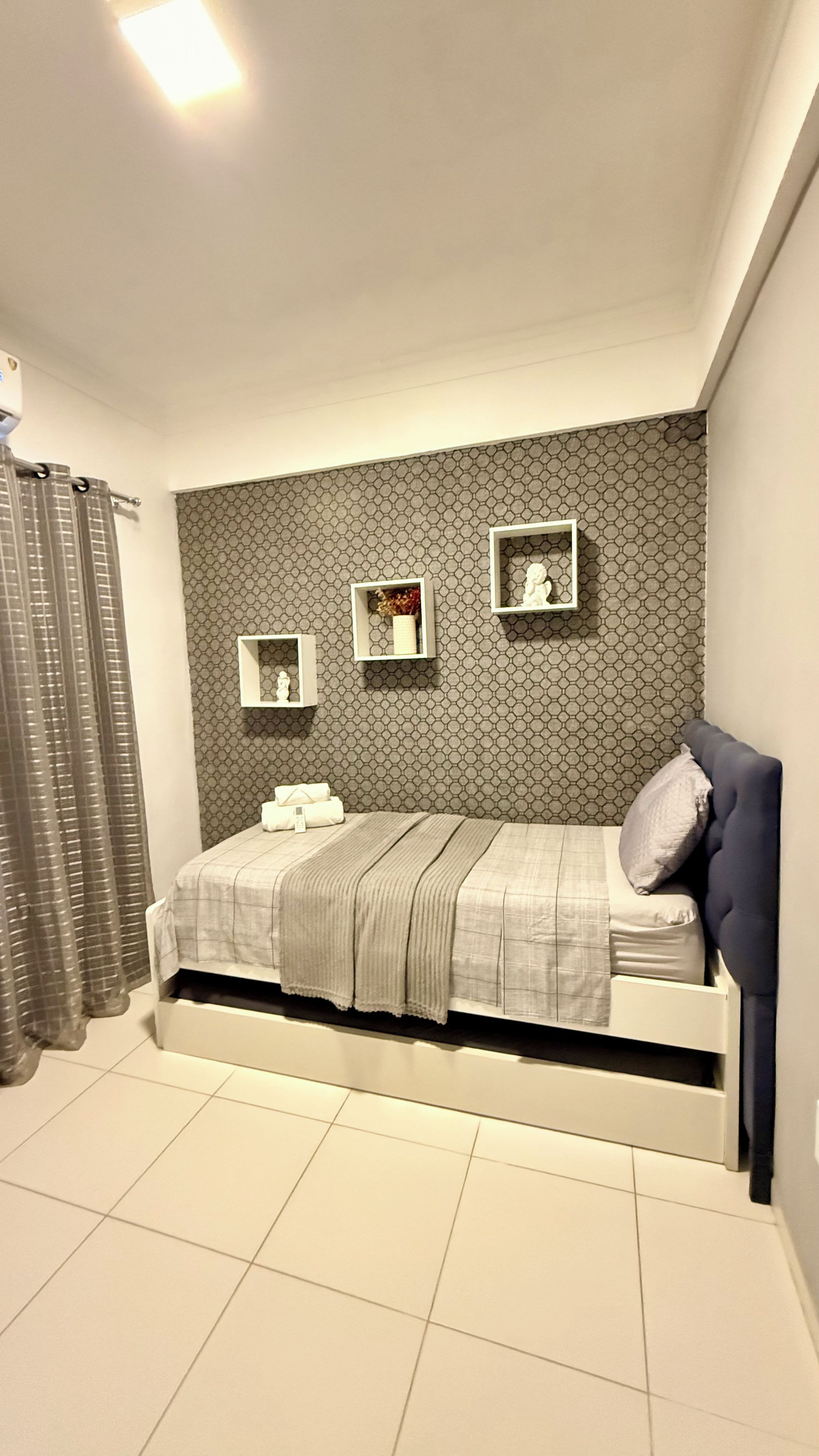 Una camera da letto con un letto, una testiera, uno scaffale a parete con oggetti decorativi e una finestra con tende.