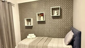 Un dormitorio con una cama, cabecera, estante en la pared y cortina.