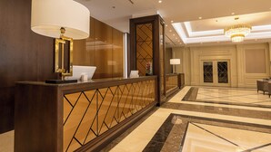 Un hall de hotel con mostrador de recepción, una araña de cristal y suelo estampado.