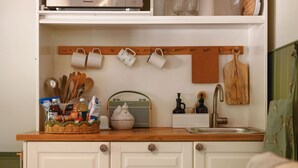 A kitchen with white cabinets, a wooden countertop, a hanging mug rack, and a vintage radio.