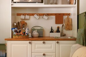 A kitchen with white cabinets, a wooden countertop, a hanging mug rack, and a vintage radio.