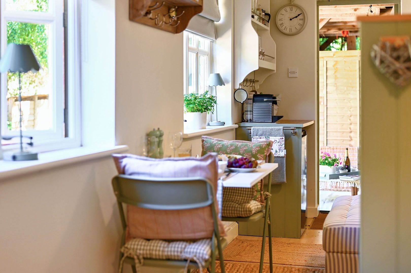 Une cuisine chaleureuse avec un coin repas, une horloge au mur et une fenêtre donnant sur un paysage verdoyant.